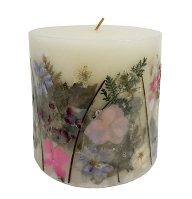 Ivory pillar candle with delicate pressed pink and purple flowers and green leaves decorating the outside of the candle.