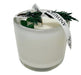 White candle cup with green stones embedded and ribbon with juniper tied on top.