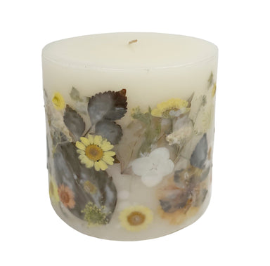 Ivory pillar candle with delicate pressed flowers in yellow and white along with green leaves decorating the outside of the candle.