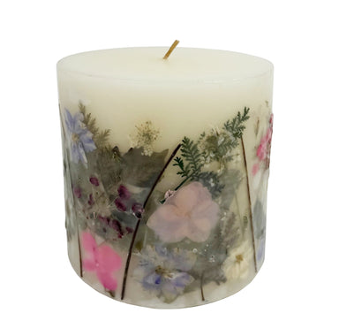 Ivory pillar candle with delicate pressed pink and purple flowers and green leaves decorating the outside of the candle.