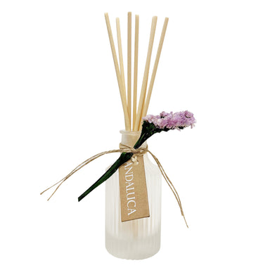 Reed diffuser with wooden sticks and a small bouquet of flowers on a white background
