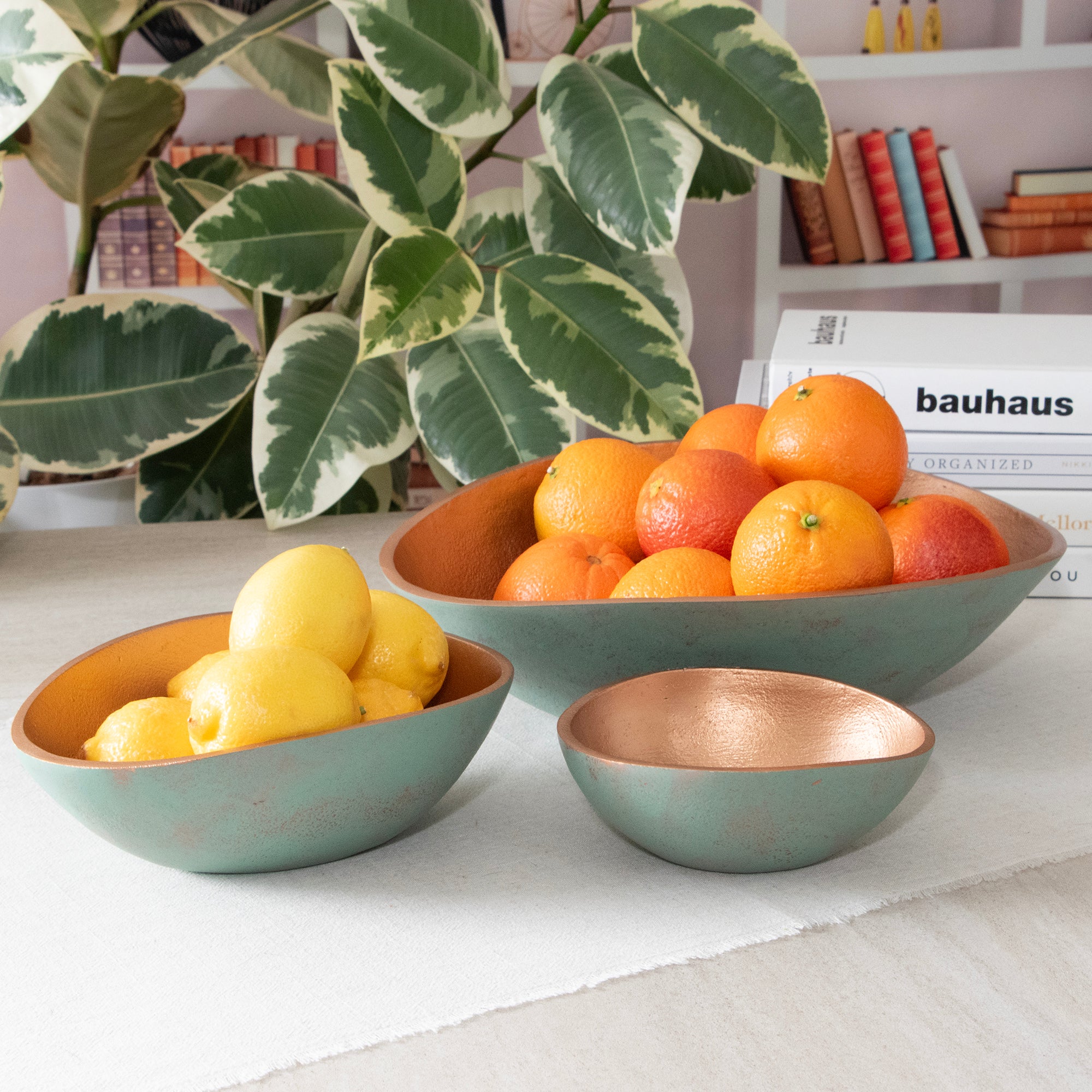 Set of 3 Turquoise Copper Cast Metal Decorative Bowls, in room setting. Large bowl filled with orange, medium bowl filled lemons, small bowl is empty. 