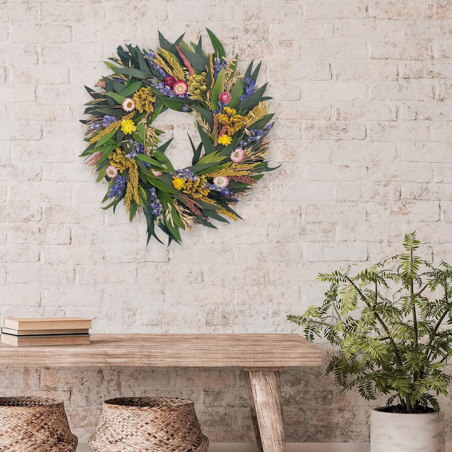 Floral wreath on a brick wall above a wooden table with a plant and books.