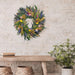 Floral wreath on a brick wall above a wooden table with a plant and books.