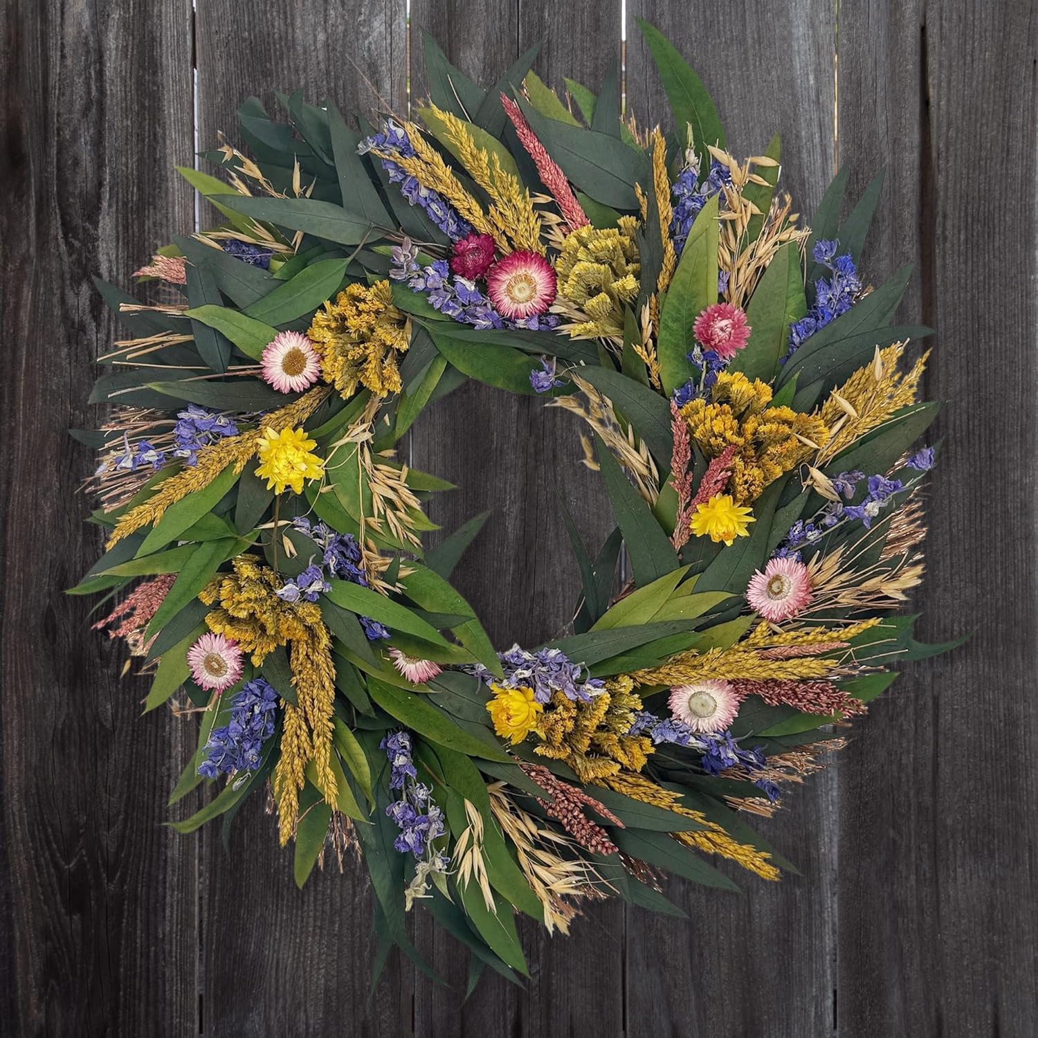 Wreath made of green leaves and colorful flowers on a wooden background
