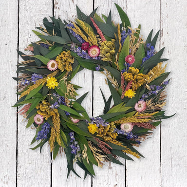 Wreath made of green leaves and colorful flowers on a white wooden background