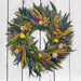 Wreath made of green leaves and colorful flowers on a white wooden background