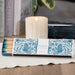 Box of decorative matches with a floral design on a table with a lit candle in the background.