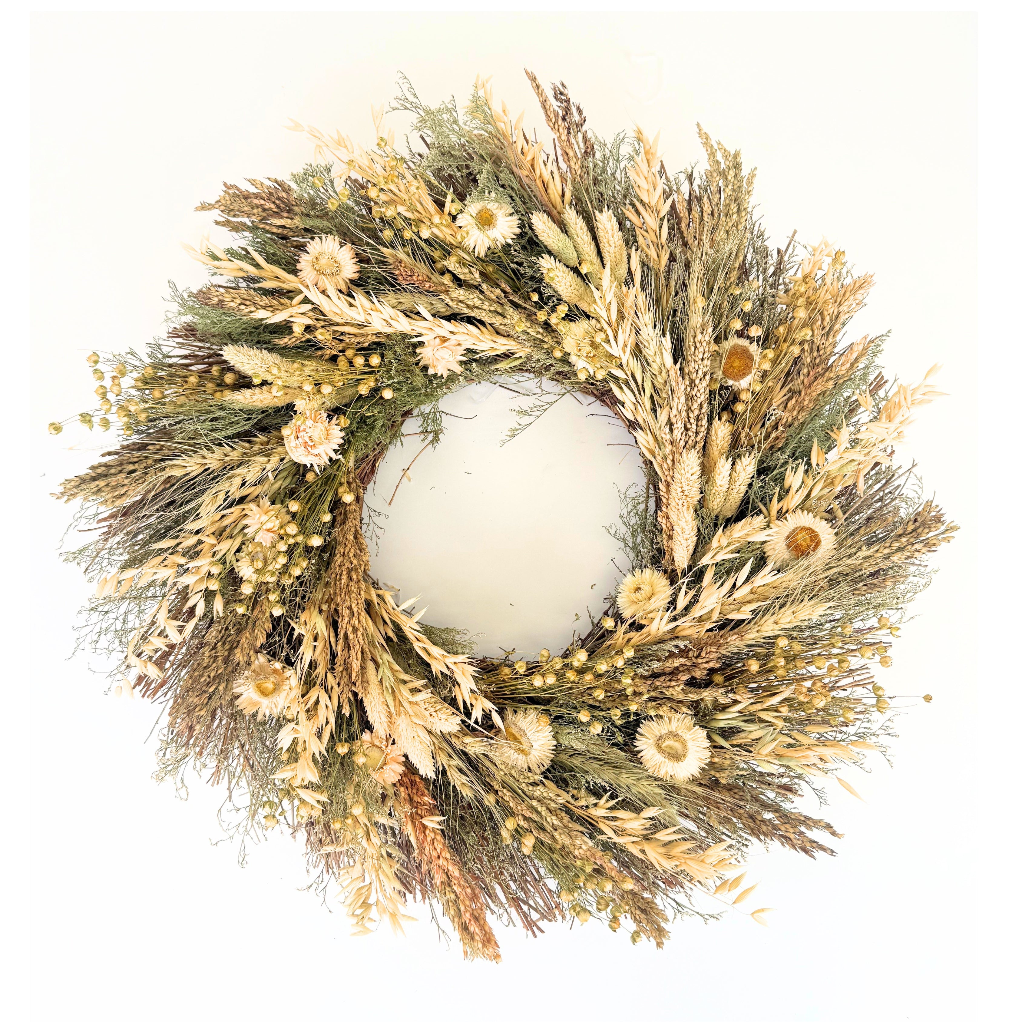 A circular dried floral wreath made of natural beige, tan, and olive green botanicals, including grasses, small flowers, and seed pods, photographed against a plain white background.