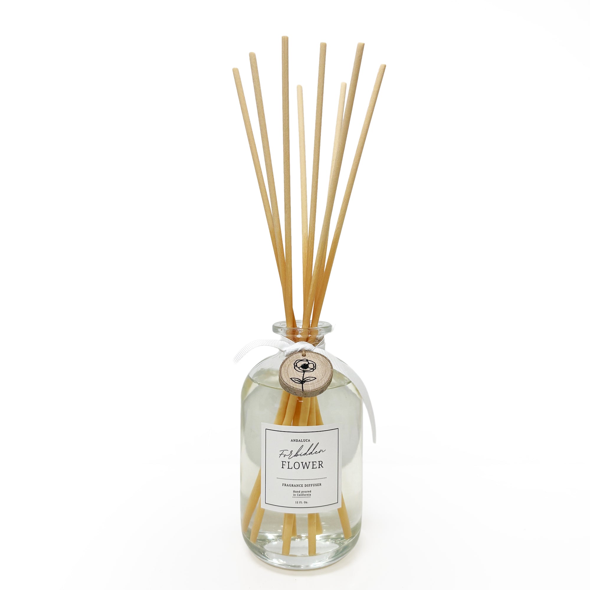 Fragrance diffuser with reeds and a wood charm tied on the neck of the glass.