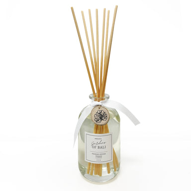 Glass bottle fragrance diffuser with reeds and wood charm tied to neck of bottle.
