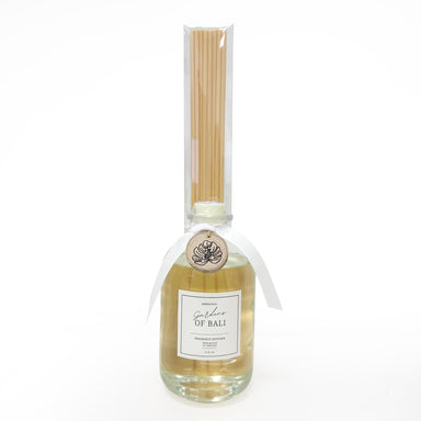 Glass bottle fragrance diffuser with reeds and wood charm tied to neck of bottle.