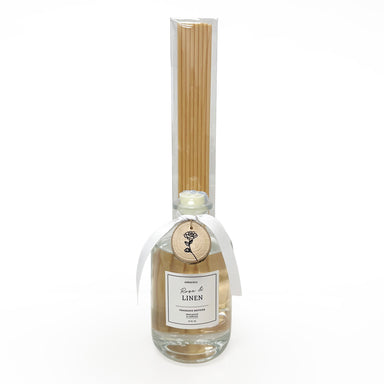 Glass reed diffuser with reeds attached to bottle and wood charm around bottle neck.