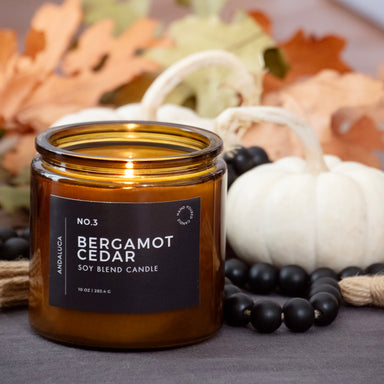 Bergamot Cedar candle in an amber jar, surrounded by autumn decorations.