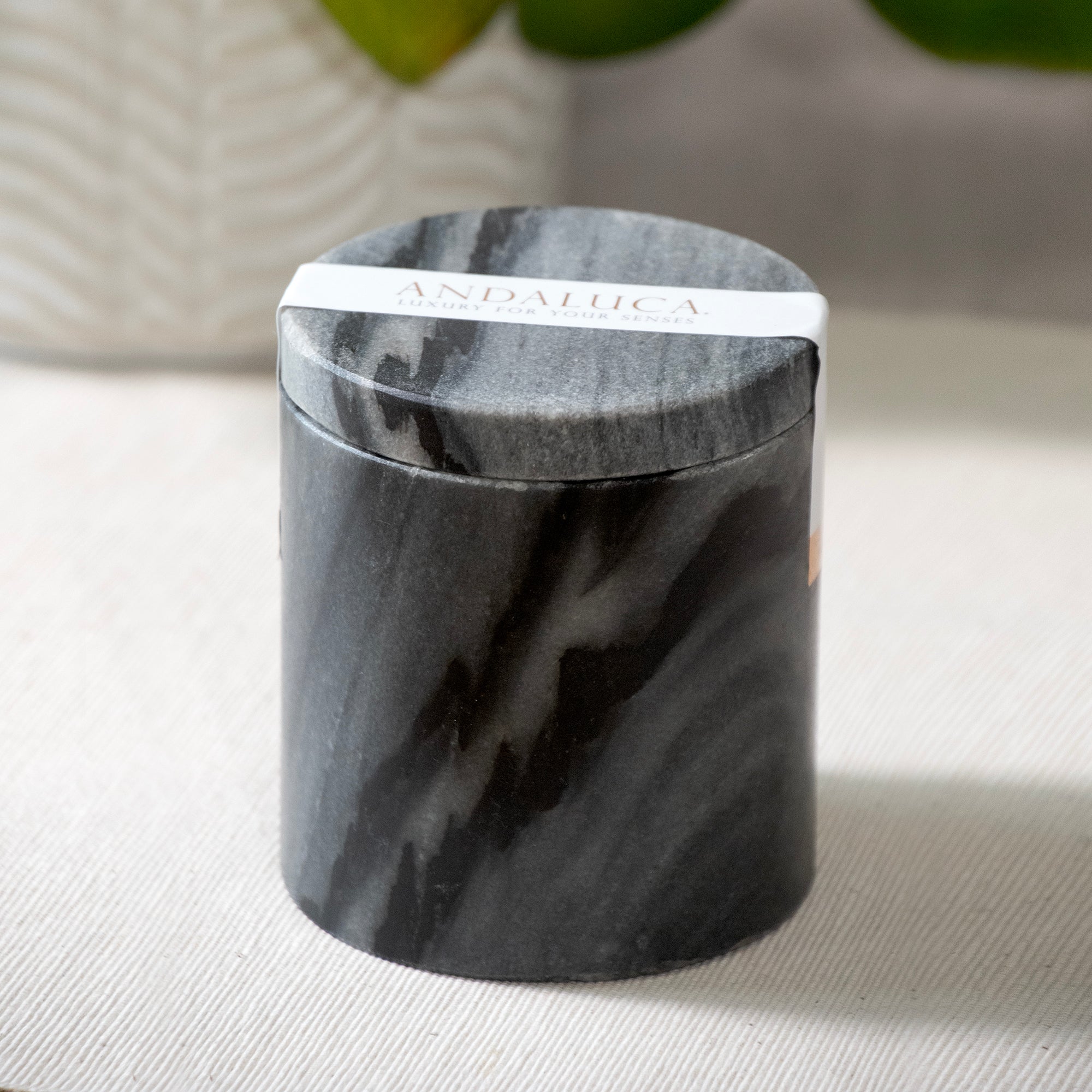 A Palo Santo Scented Black Marble Candle, closed lid with label on, sitting on a table top.