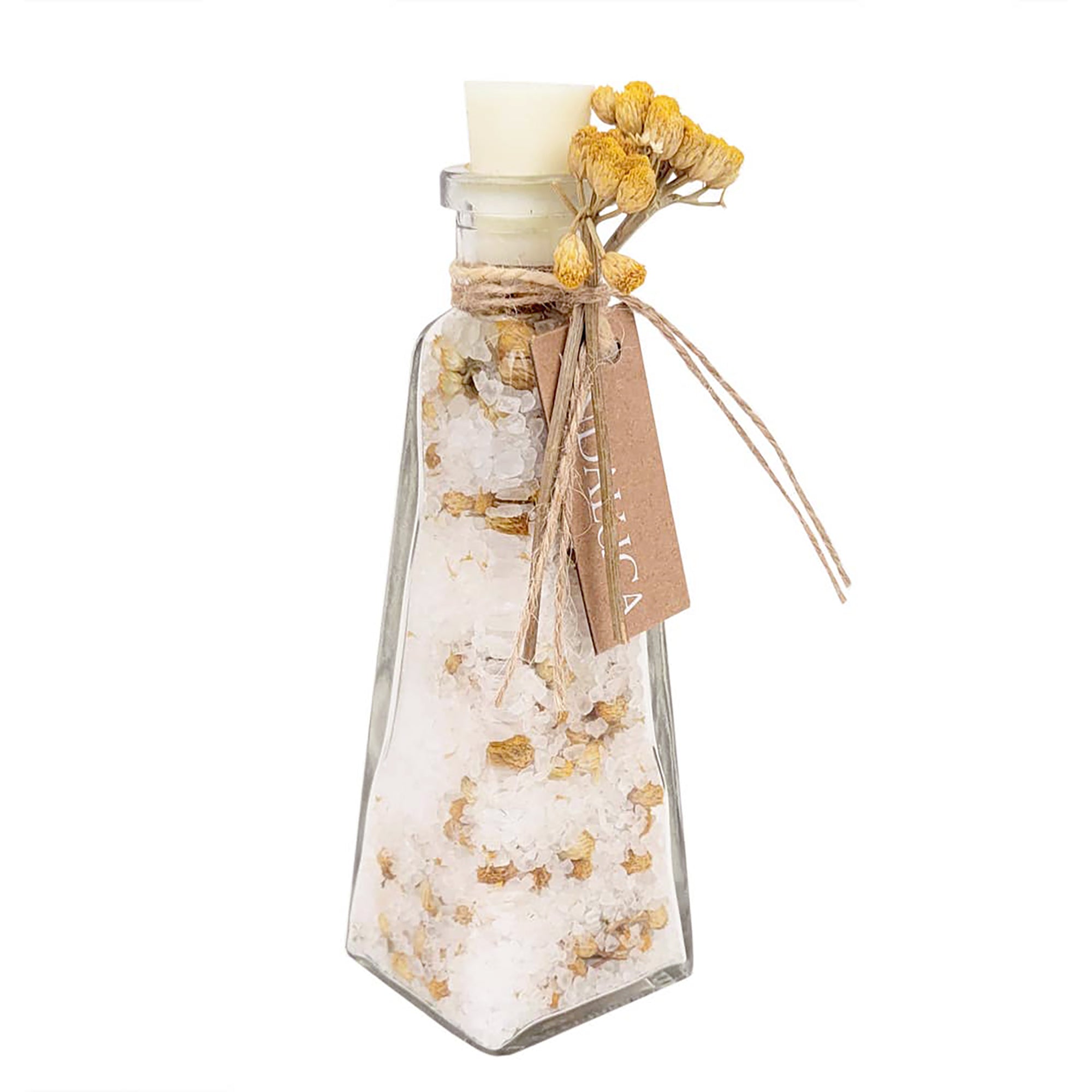 A clear glass bottle with a pointed bottom, filled with white bath salts or sugar crystals mixed with dried yellow flowers. The bottle is sealed with a white stopper, tied with twine, and has a kraft paper tag attached, all on a plain white background.
