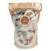 A clear resealable stand-up pouch with a kraft paper top, filled with coarse white crystals and dried botanicals including green leaves and dried citrus slices, photographed on a plain white background.