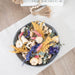 Decorative plate with dried flowers on a light wooden surface