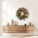 Gold Patina Wreath hanging  on a wall above a wooden floating cabinet with decorative items on it.