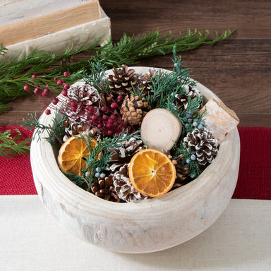 Close up of Holiday Memories Burlap Pinecone bag is displaed in a white wood bowl. Shot in a room setting with an open small journal with pen on it.