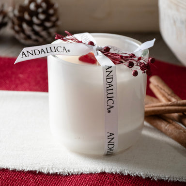 White glass candle vessel packaged with Andaluca branded white ribbon and dried botanical red berrys. Shot in a room setting.