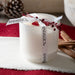 White glass candle vessel packaged with Andaluca branded white ribbon and dried botanical red berrys. Shot in a room setting.