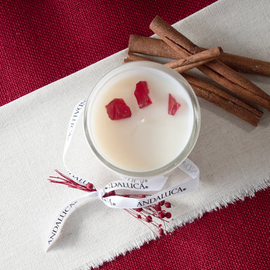 Top veiw, of the white glass candle vessel with packaging tie off to the side. Showing the 3 simi transpartent red stones embedded in the wax top of the candle. Stones do not need to be removed before burning.  Shot on a table top room setting.