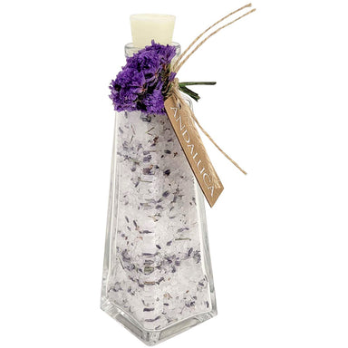 A clear glass bottle filled with white bath salts and dried lavender buds, topped with a white wax seal and decorated with a purple flower sprig, twine, and a hanging tag reading 'ANIMALUCY'.