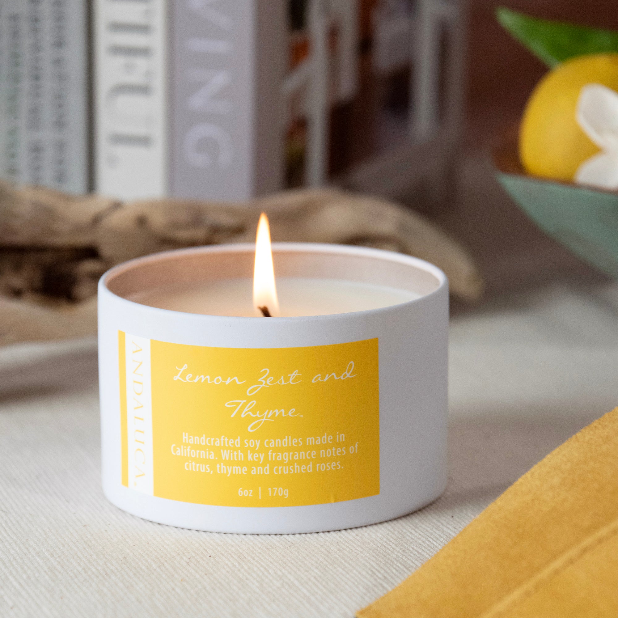 Lemon Zest and Thyme tin candle, burning, on a table.