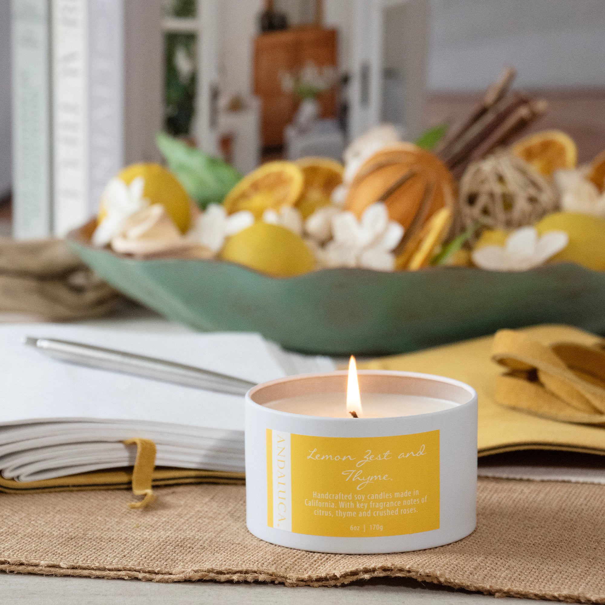 Lemon Zest and Thyme tin candle, burning, on a table.