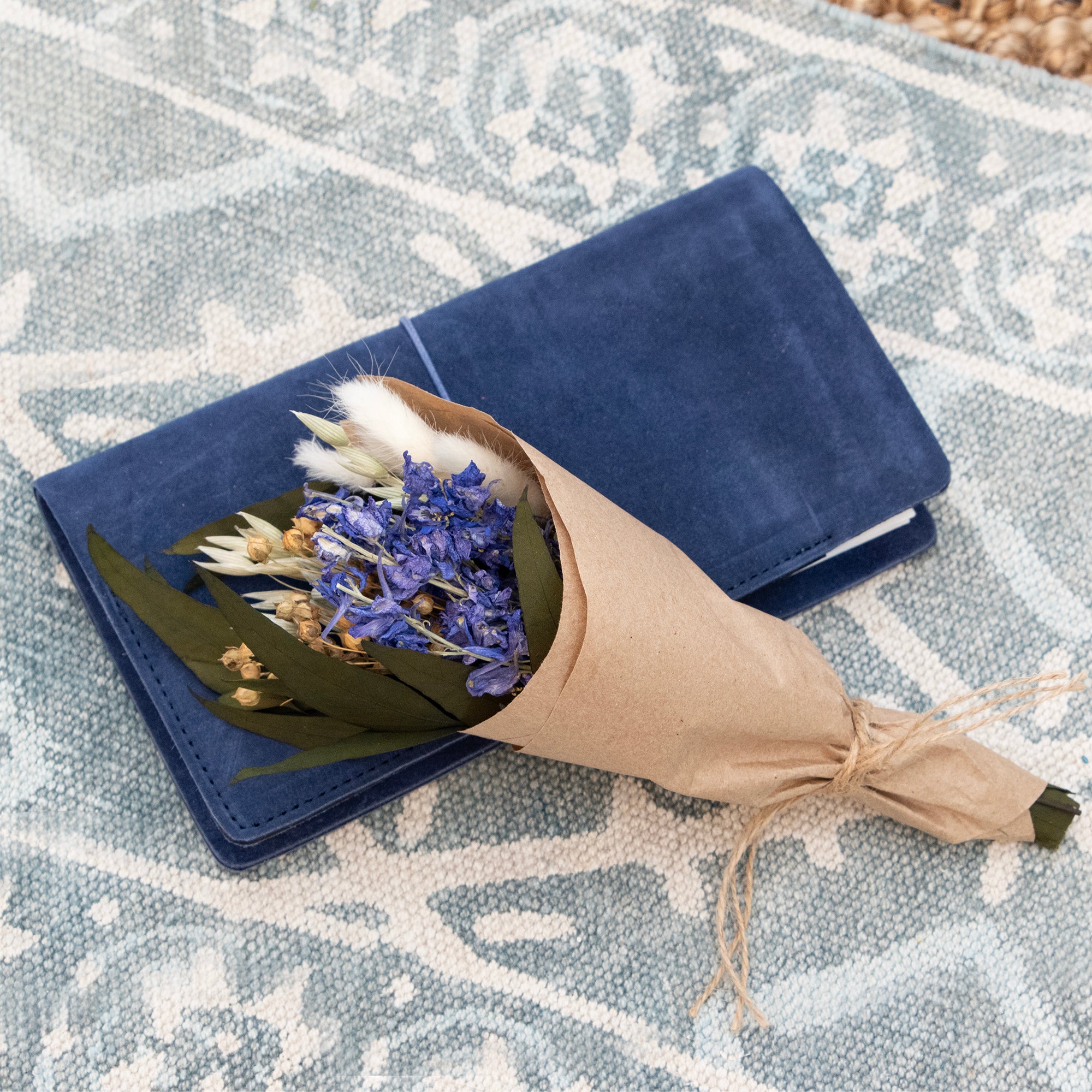 Mini bouquet with purple larkspur, willow eucalyptus, bunny tails, flax, and aveena laid on top of a journal.