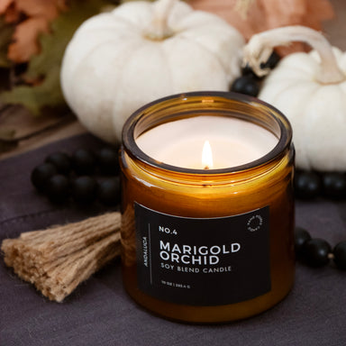 Marigold Orchid burning candle with pumpkins and leaves in the background.