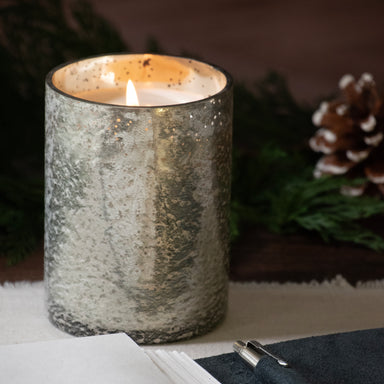 Mercury candle cup lit, set on a table top with a note book infront of it.