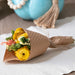 Bouquet of yellow flowers wrapped in brown paper on a white surface with a blue pumpkin in the background.
