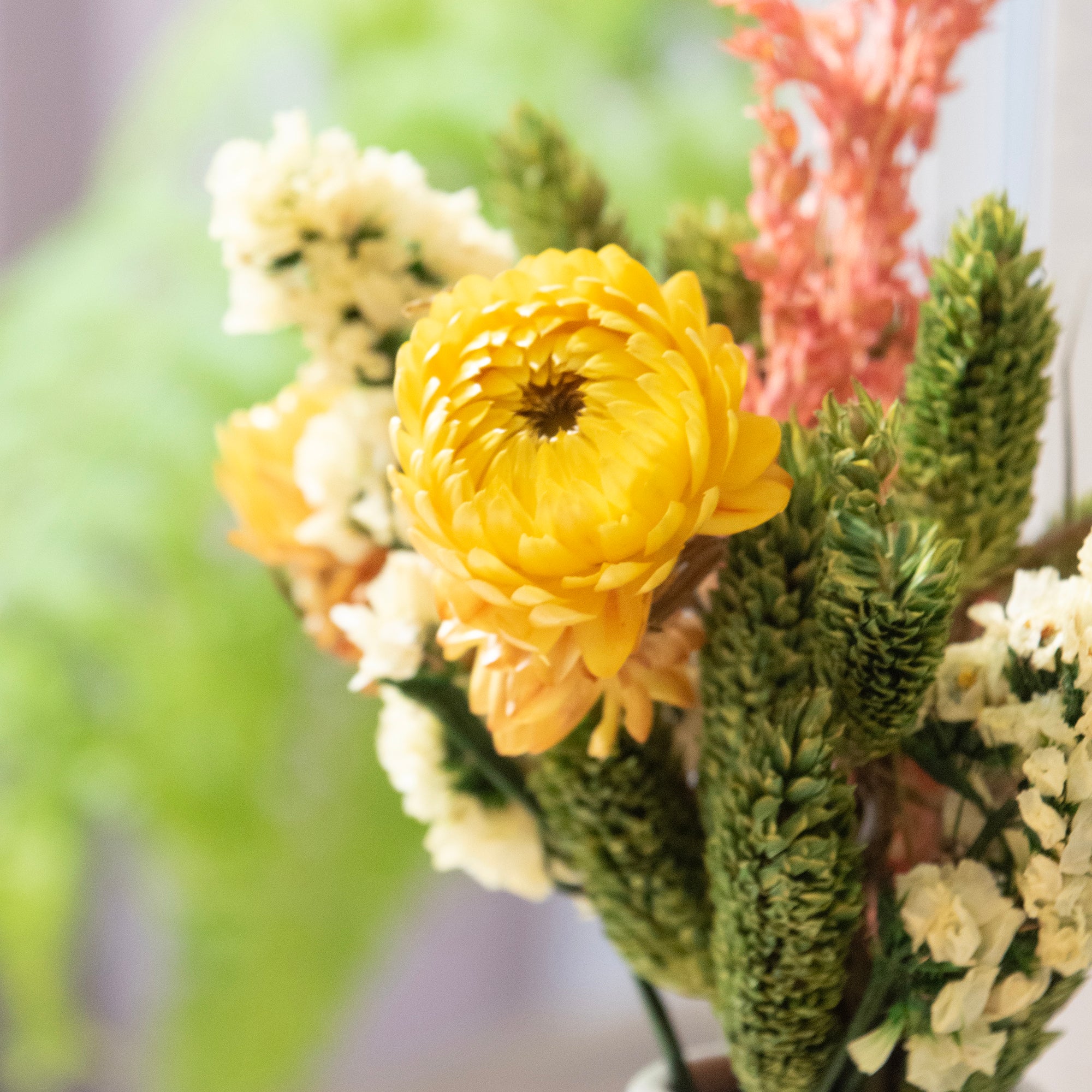 Bouquet of flowers with a yellow flower in the center, surrounded by greenery and white flowers.