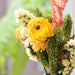 Bouquet of flowers with a yellow flower in the center, surrounded by greenery and white flowers.