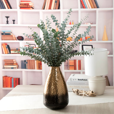 Ombre Cast Metal Bronze Decorative Vase, in a room setting. Fresh Baby Eucalyptus in the vase.