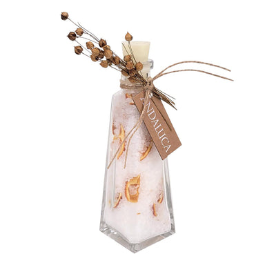A clear glass bottle with a pointed bottom, filled with white wax or resin and decorated with dried botanical elements. The bottle is sealed with a small cream-colored stopper and tied with twine, featuring a hanging tag that reads 'ANDALUCA' and dried flower stems at the top, all on a plain white background.