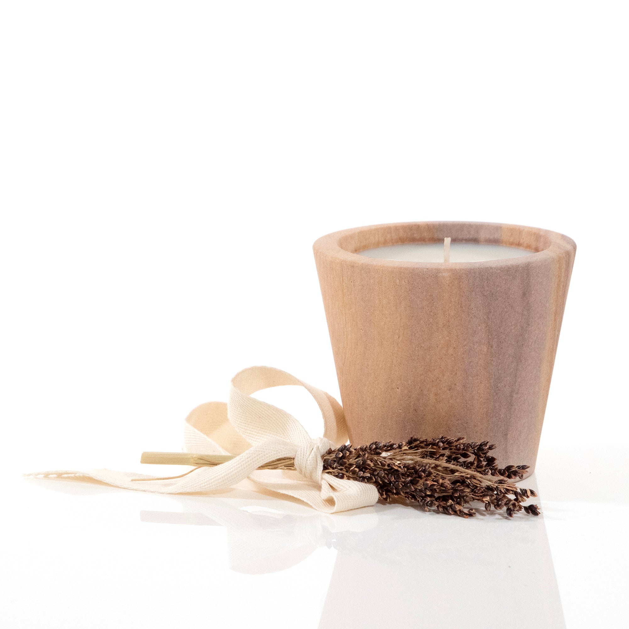 Travertine candle cup with ribbon and botanical on the table.