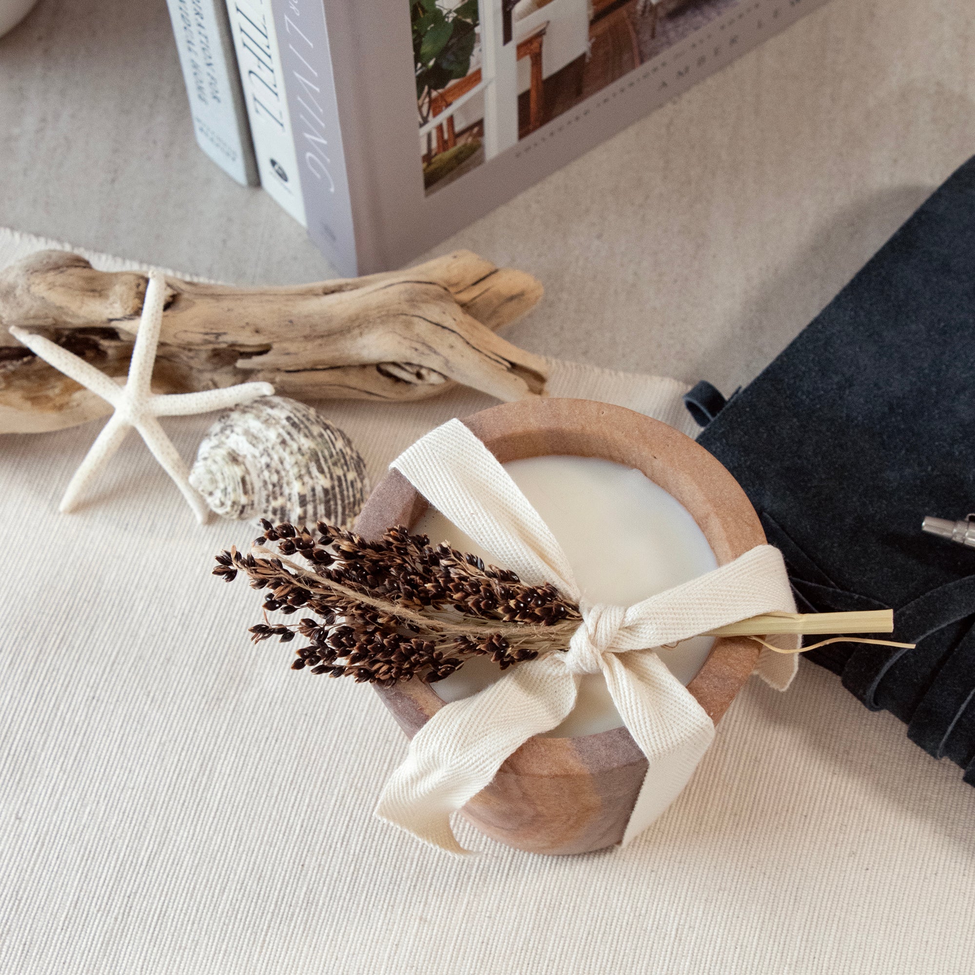 Travertine candle cup with ribbon and botanical on a decorative table.