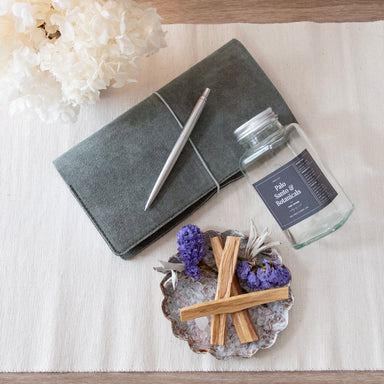 Product jar emptied to show contents, poured into a textured metal dish. All placed onto a table surface also displaying a Gray notebook with pen and white hydrangeas.