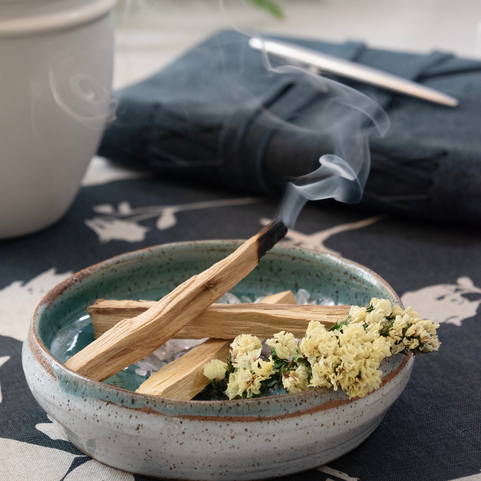 Contents of the Palo Santo & Yellow Flower Smudging Jar Set, displayed in a ceramic dish with a burning palo Santo stick.