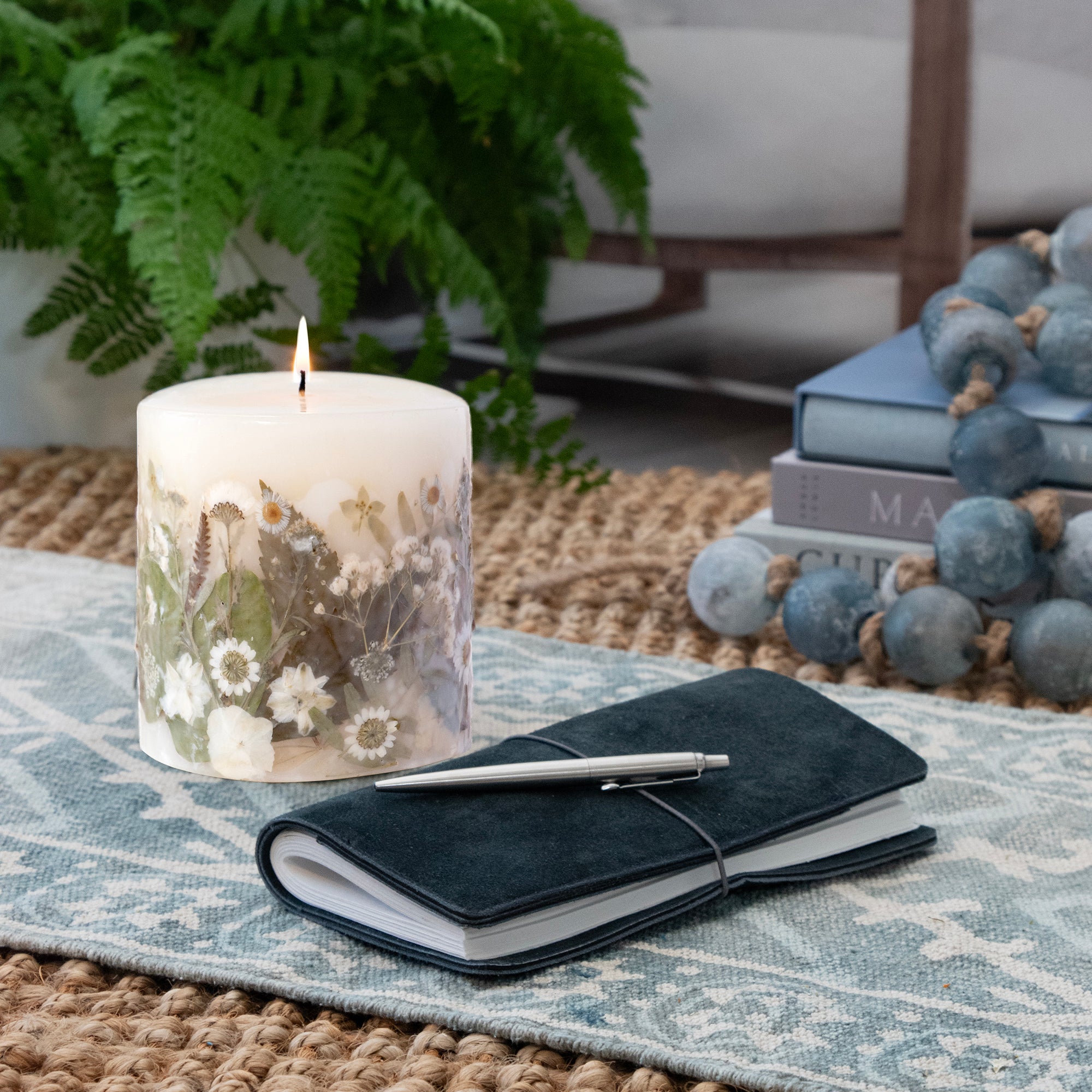 Ivory pillar candle with delicate white pressed flowers and green leaves decorating the outside of the candle.