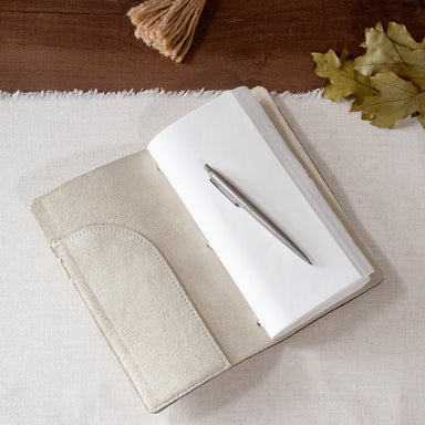 Beige suede journal, open on a table. showing a pen that does not come with it.