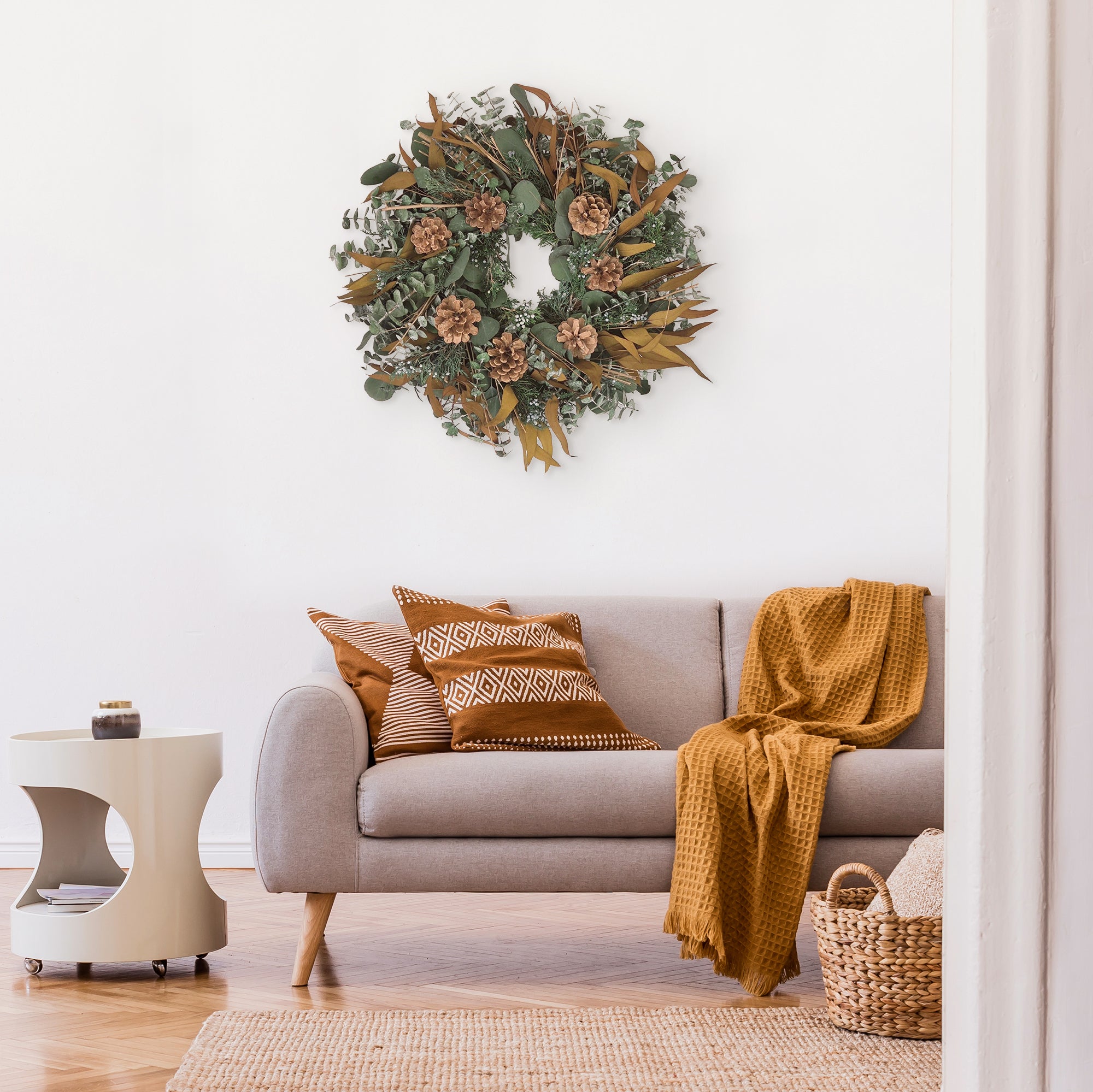 Decorative wreath with greenery, pinecones, and brown leaves in a room setting.
