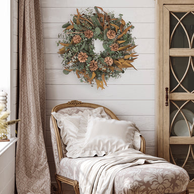 Decorative wreath with greenery, pinecones, and brown leaves in a room setting.