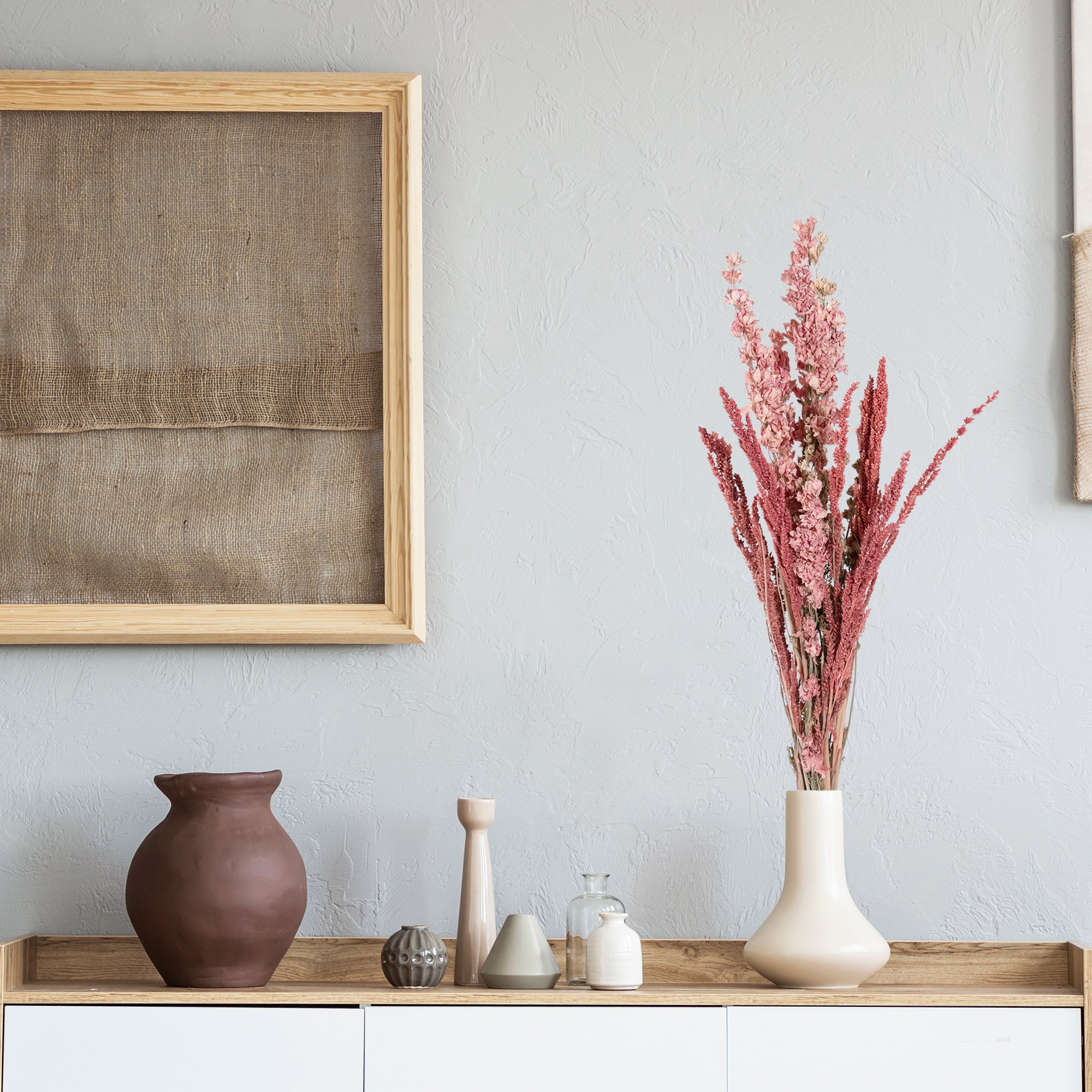 Pink floral bouquet with grains wrapped in brown paper in vase.