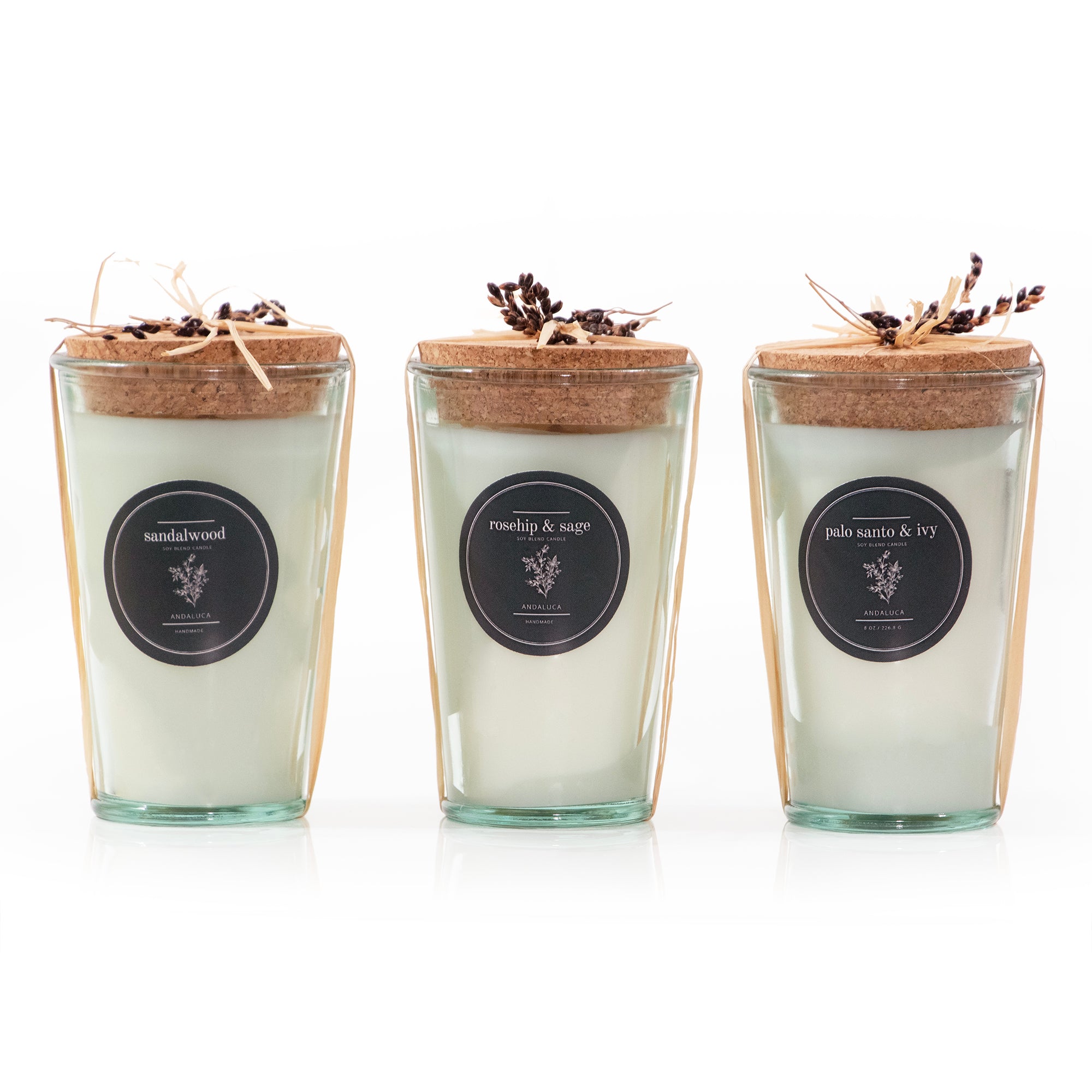 All three candle fragrance shown together. They are candles poured in a recycled glass vessel with thick cork cap, tied with a raffia tie and botanical sprig. 