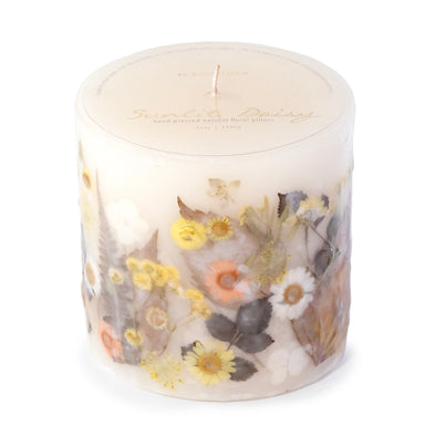 Ivory pillar candle with delicate pressed flowers in yellow and white along with green leaves decorating the outside of the candle.