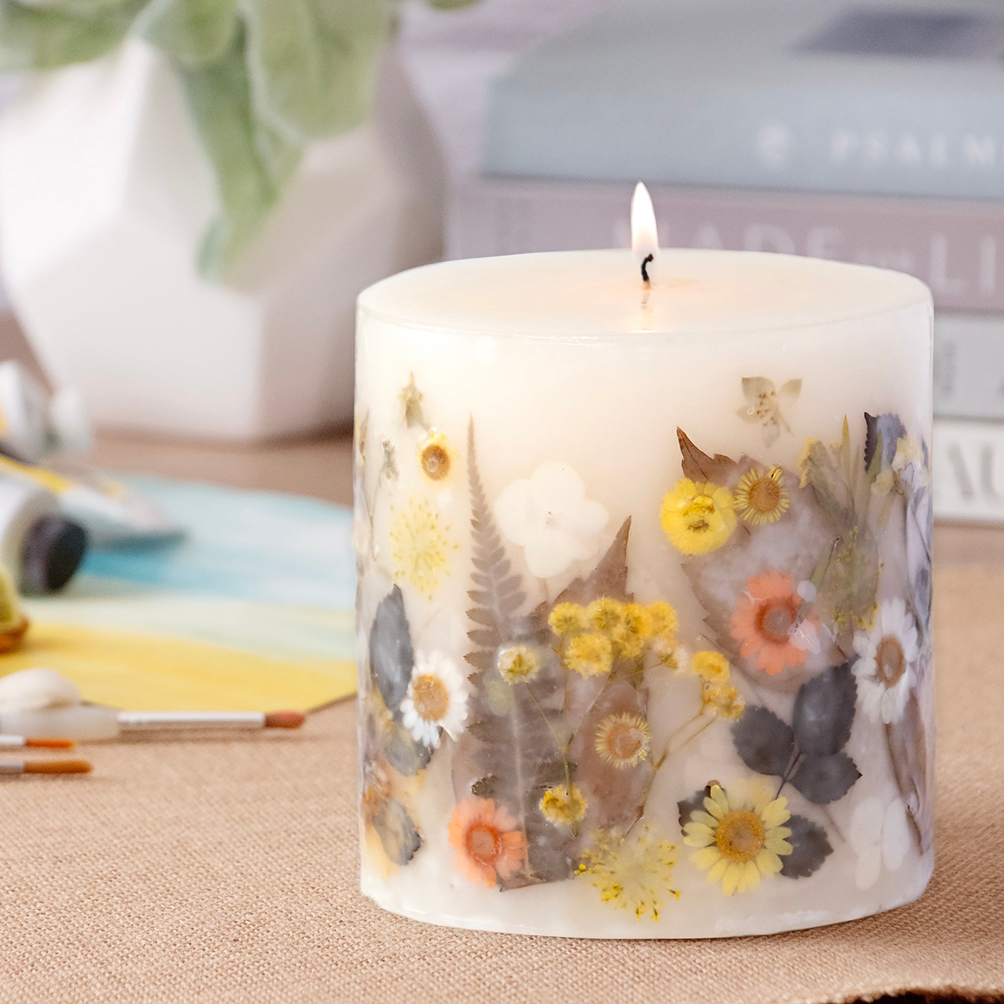 Ivory pillar candle with delicate pressed flowers in yellow and white along with green leaves decorating the outside of the candle.